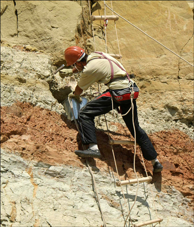 A scientist carefully works away at the rock face.
