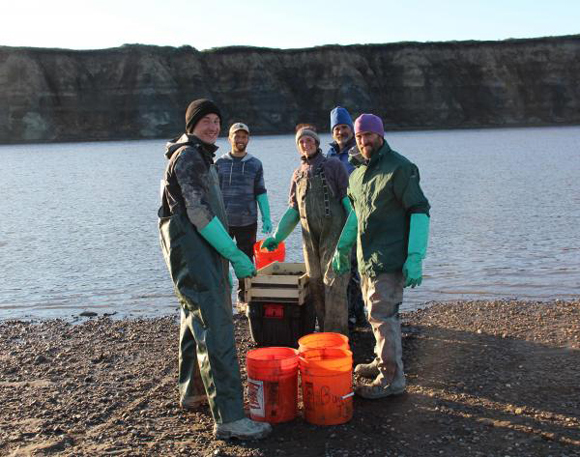Researchers pose next to buckets of sediments that will be sieved for microfossils.